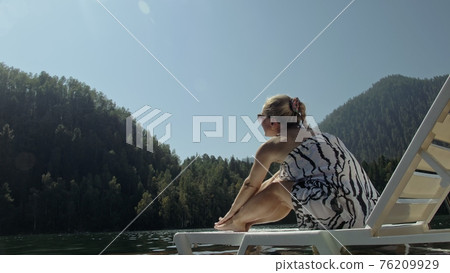 Woman lie on a sunbed in sunglasses and a boho silk shawl. Girl rest on a flood wood underwater pier. The pavement is covered with water in the lake. Woman lie on a sunbed in sunglasses and a boho silk shawl. Girl rest on a flood wood underwater pier. The pavement is covered with water in the lake. 76209929