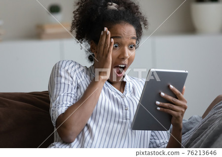 Amazed biracial woman shocked by unexpected message on tablet 76213646