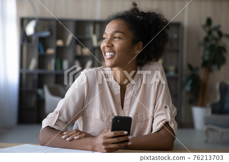 Smiling African American woman use cellphone dreaming 76213703