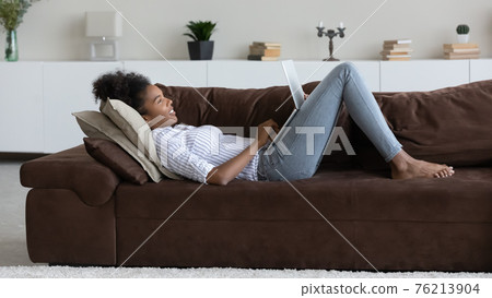 Young biracial woman rest on sofa using laptop Young biracial woman rest on sofa using laptop 76213904
