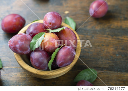 Ripe plums and leaves in a wooden bowl on the table. 76214277