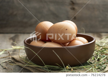 Fresh chicken eggs in a clay bowl on the hay. 76214278