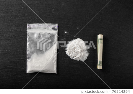 Cocaine in a plastic package on a black background, close-up. A rolled up dollar bill for drug use. Cocaine in a plastic package on a black background, close-up. A rolled up dollar bill for drug use. 76214294