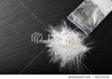Cocaine in a plastic package on a black background, close-up. Cocaine in a plastic package on a black background, close-up. 76214316