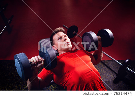 A sporty blond man doing exercises with dumbbells in the gym A sporty blond man doing exercises with dumbbells in the gym 76214474