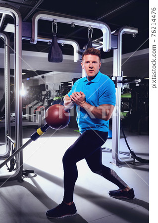 A sporty blond man doing exercises with a ball in the gym A sporty blond man doing exercises with a ball in the gym 76214476