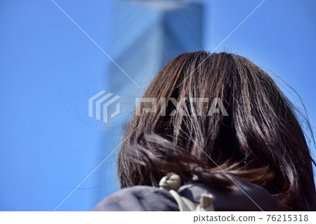 A woman looking up at a building under the blue sky A woman looking up at a building under the blue sky 76215318
