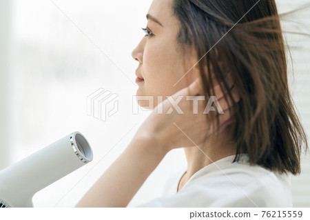 Young woman using a hairdryer in the washroom 76215559