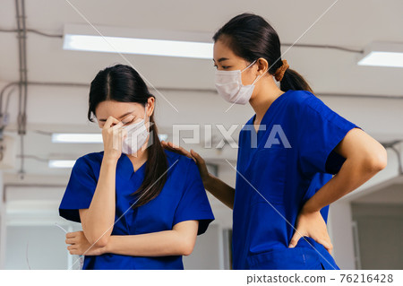 Young nurse comforting colleague wearing mask Young nurse comforting colleague wearing mask 76216428