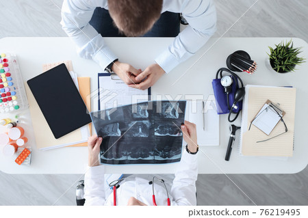 Doctor and patient are discussing the X-ray at work table 76219495