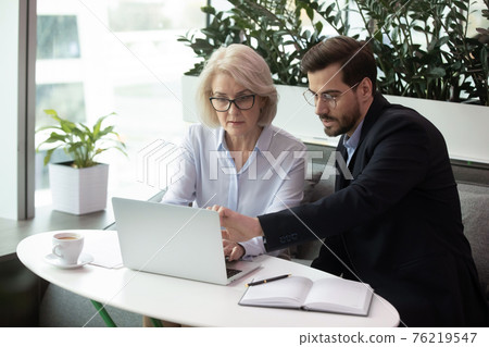 Diverse employees work on laptop in office together Diverse employees work on laptop in office together 76219547