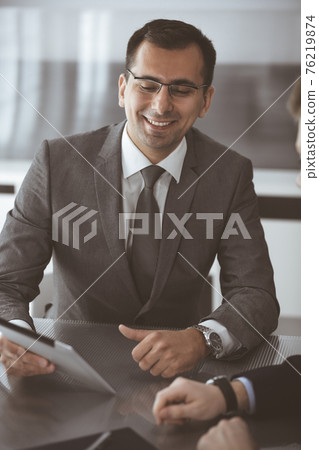 Businessman headshot at meeting in modern office. Entrepreneur sitting at the table with colleagues. Teamwork and partnership concept. Grey blazer suits to happy smiling manager Businessman headshot at meeting in modern office. Entrepreneur sitting at the table with colleagues. Teamwork and partnership concept. Grey blazer suits to happy smiling manager 76219874