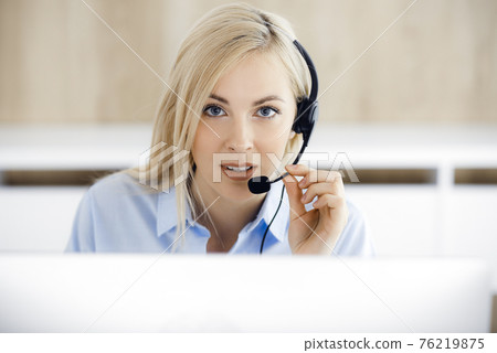 Blonde business woman sitting and communicated by headset in call center office. Concept of telesales business or home office occupation Blonde business woman sitting and communicated by headset in call center office. Concept of telesales business or home office occupation 76219875