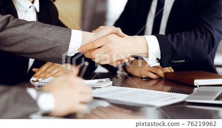 Unknown businessman shaking hands with his colleague or partner above the glass desk in modern office, close-up. Business people group at meeting Unknown businessman shaking hands with his colleague or partner above the glass desk in modern office, close-up. Business people group at meeting 76219962
