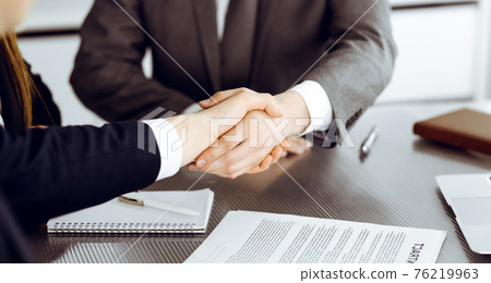 Unknown businessman shaking hands with his colleague or partner above the glass desk in modern office, close-up. Business people group at meeting 76219963