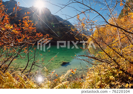 Mountain lake with transparent water and colorful autumnal trees. Mountains and crystal lake Mountain lake with transparent water and colorful autumnal trees. Mountains and crystal lake 76220104