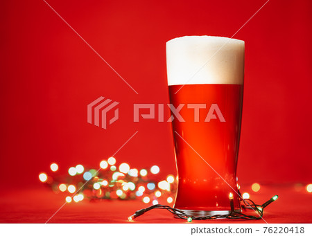 Pale ale or beer in pint glass with christmas lights on red background Pale ale or beer in pint glass with christmas lights on red background 76220418