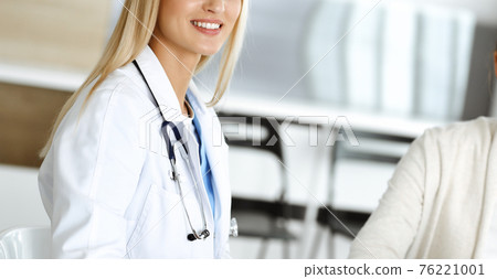 Woman-doctor sitting and communicating with her female patient in clinic. Blonde physician happy to help. Medicine concept 76221001