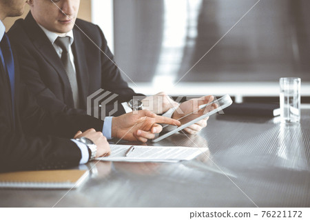 Unknown businessmen using tablet computer and work together at the glass desk in modern office, close-up. Teamwork and partnership concept 76221172