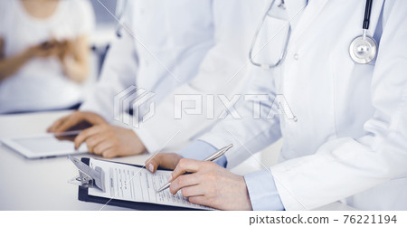 Unknown woman-doctors at work with patient at the background. Female physicians filling up medical documents or prescription while standing in hospital reception desk, close-up. Health care concept Unknown woman-doctors at work with patient at the background. Female physicians filling up medical documents or prescription while standing in hospital reception desk, close-up. Health care concept 76221194