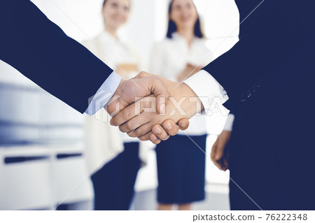 Businessman and woman shaking hands with colleagues at the background. Handshake at meeting in office. Concept of success in business Businessman and woman shaking hands with colleagues at the background. Handshake at meeting in office. Concept of success in business 76222348