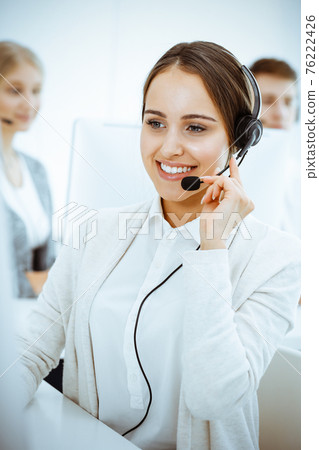 Call center. Group of diverse operators at work. Beautiful woman in headset communicating with customers of telemarketing service. Business concept 76222426