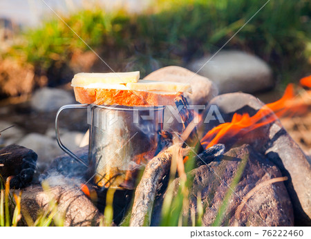 Warming up a cup of tea with sandwich at campfire outdoor Warming up a cup of tea with sandwich at campfire outdoor 76222460