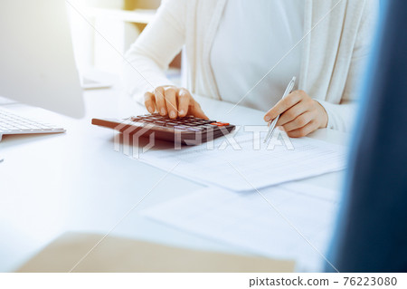 Accountant checking financial statement or counting by calculator income for tax form, hands closeup. Business woman sitting and working with colleague at the desk in office. Tax and Audit concept 76223080