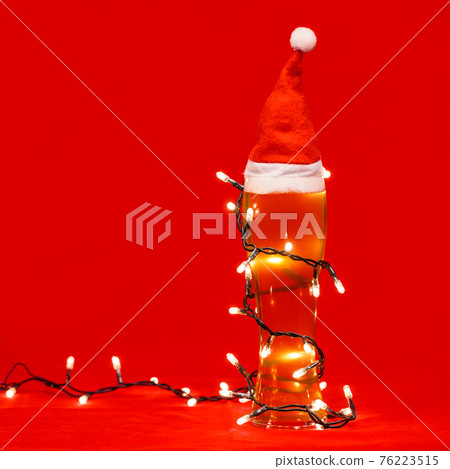 Tall glass of pale ale or beer with red santa hat and lights - christmas drink background Tall glass of pale ale or beer with red santa hat and lights - christmas drink background 76223515