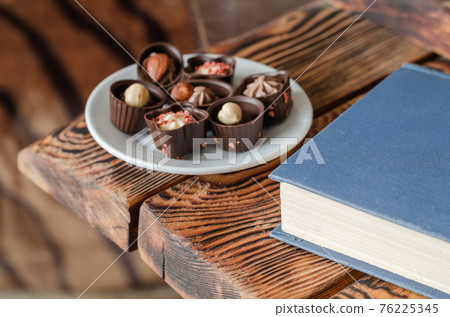 Closeup of tasty candies on a wooden table next to a closed book 76225345