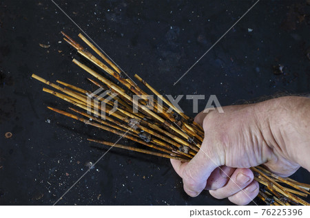 Man's hand holds group of dirty bamboo skewers with leftover food. 76225396