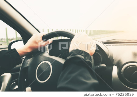 Close-up on male hands on the steering wheel of a car on a blurred background of the highway. Image with modified tones, vintage effect. Close-up on male hands on the steering wheel of a car on a blurred background of the highway. Image with modified tones, vintage effect. 76226059