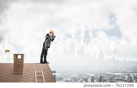 Engineer man standing on roof and looking in binoculars. Mixed m Engineer man standing on roof and looking in binoculars. Mixed m 76227208