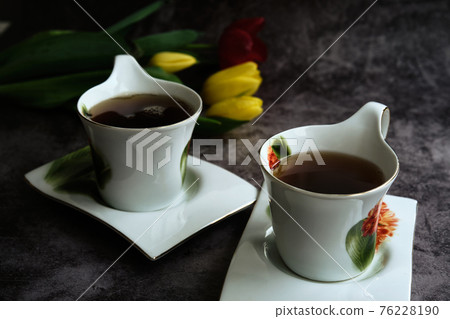 two white cups of tea and yellow and red tulips 76228190