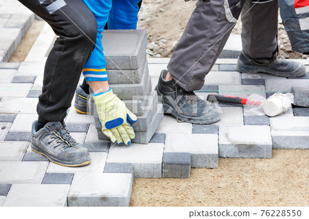 A worker wearing work gloves brings paving slabs to a paving work site. 76228550