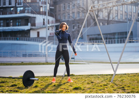 Young woman exercising with a kettlebell outside at stadium Young woman exercising with a kettlebell outside at stadium 76230076