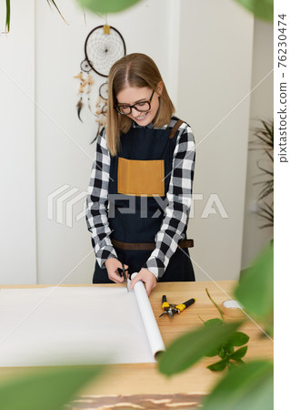 florist woman cutting paper on table with plants. florist woman cutting paper on table with plants. 76230474