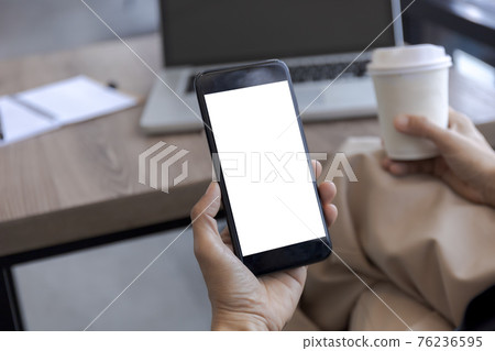 Top view female hands holding smart phone with blank white screen. Women hands workspace, close-up hand holding smartphone blank screen for text and content at cafe coffee shop Top view female hands holding smart phone with blank white screen. Women hands workspace, close-up hand holding smartphone blank screen for text and content at cafe coffee shop 76236595
