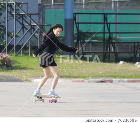 Asian women play surf skates board outdoors on beautiful summer day. Happy young women play surfskate at park on morning time. Sport activity lifestyle concept. Young women enjoy with SurfSkate board 76236599