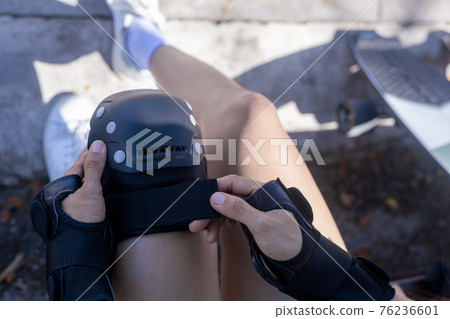 top view Close up Woman surf skate board putting on knee protector pads on her arm and wearing wrist guards. On morning young women puting protective guard before play surf skate board. top view Close up Woman surf skate board putting on knee protector pads on her arm and wearing wrist guards. On morning young women puting protective guard before play surf skate board. 76236601
