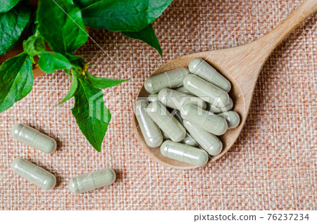 Pile of herbal medicine capsules in wooden spoon with green leaf. Pile of herbal medicine capsules in wooden spoon with green leaf. 76237234