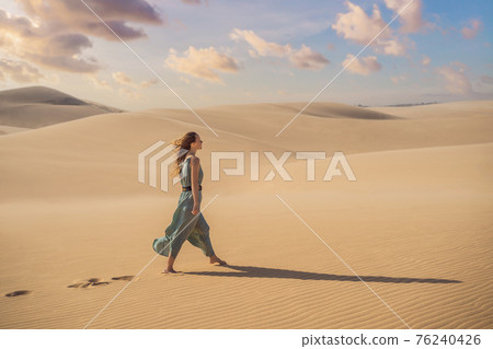 Young beautiful woman traveling in the desert. Sandy dunes and blue sky on sunny summer day. Travel, adventure, freedom concept. Tourism reopens after quarantine COVID 19 76240426