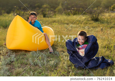 two boys are having fun in nature, one sits on a lamzak, the other in a sleeping bag, a fun morning two boys are having fun in nature, one sits on a lamzak, the other in a sleeping bag, a fun morning 76241014