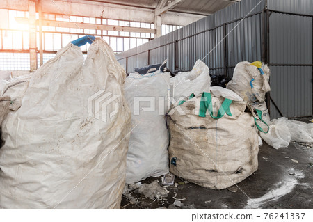 Heap of many dirty big bag containers with used water pet bottles collected for recyclyng and reuse at abandoned recycling factory warehouse. Environmental protection from pollution 76241337
