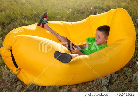 little boy lies in a lamzak, holding a smartphone or tablet in his hands, plays or communicates on social networks little boy lies in a lamzak, holding a smartphone or tablet in his hands, plays or communicates on social networks 76241622