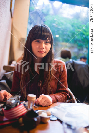A long-haired woman with a film camera on the table inside a cafe 76242886