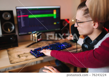 Woman put finger on keyboard and help for man in his work. Process of freelancer working at home. Man using professional microphone and headphones Woman put finger on keyboard and help for man in his work. Process of freelancer working at home. Man using professional microphone and headphones 76243224
