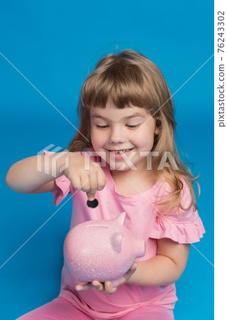 happy girl, in pink clothes, with a pink piggy bank, smiles and puts a coin in the piggy bank, finance and accumulation concept happy girl, in pink clothes, with a pink piggy bank, smiles and puts a coin in the piggy bank, finance and accumulation concept 76243302