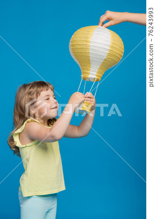 little girl touches yellow balloon, hands raised, looks and smiles, concept of adventure and fantasy 76243993
