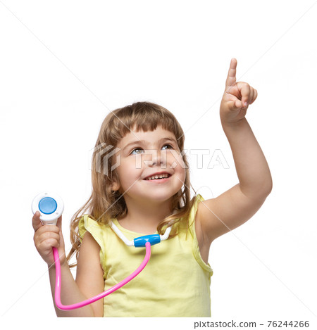 cheerful little girl with a phonendoscope in her hand, the second hand indicates the place where the inscription may be, the concept of medicine and health, emotions, on a white background 76244266
